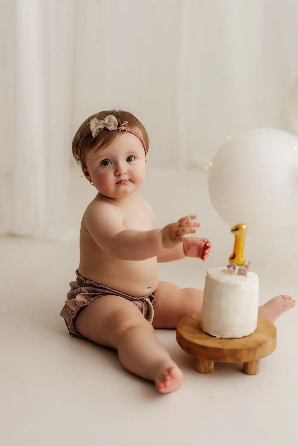 Narodeninove_fotenie_v_atelieri (3) Dievčatko sedí a naťahuje sa za jednotkou ktorá je zapychnutá v narodeninovej torte počas narodeninového fotenia v ateliéri v Šuranoch
