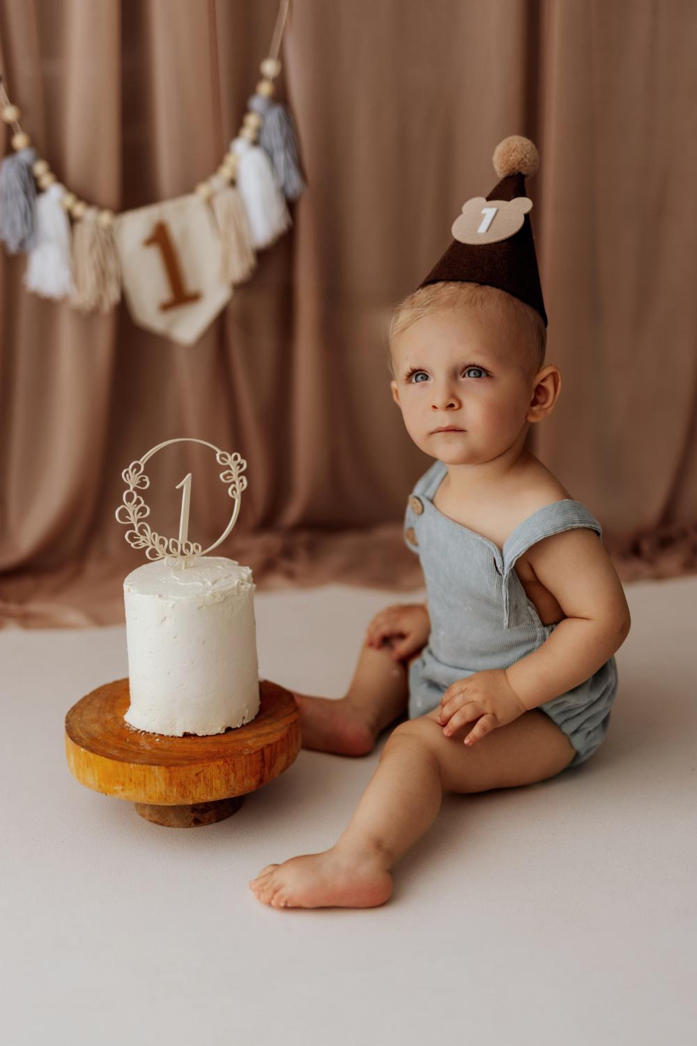  Dieťa sa zvedavo pozerá pričom sedí vedľa tortky počas cake smash narodeninového fotenia v ateliéri v Nových Zámkoch 