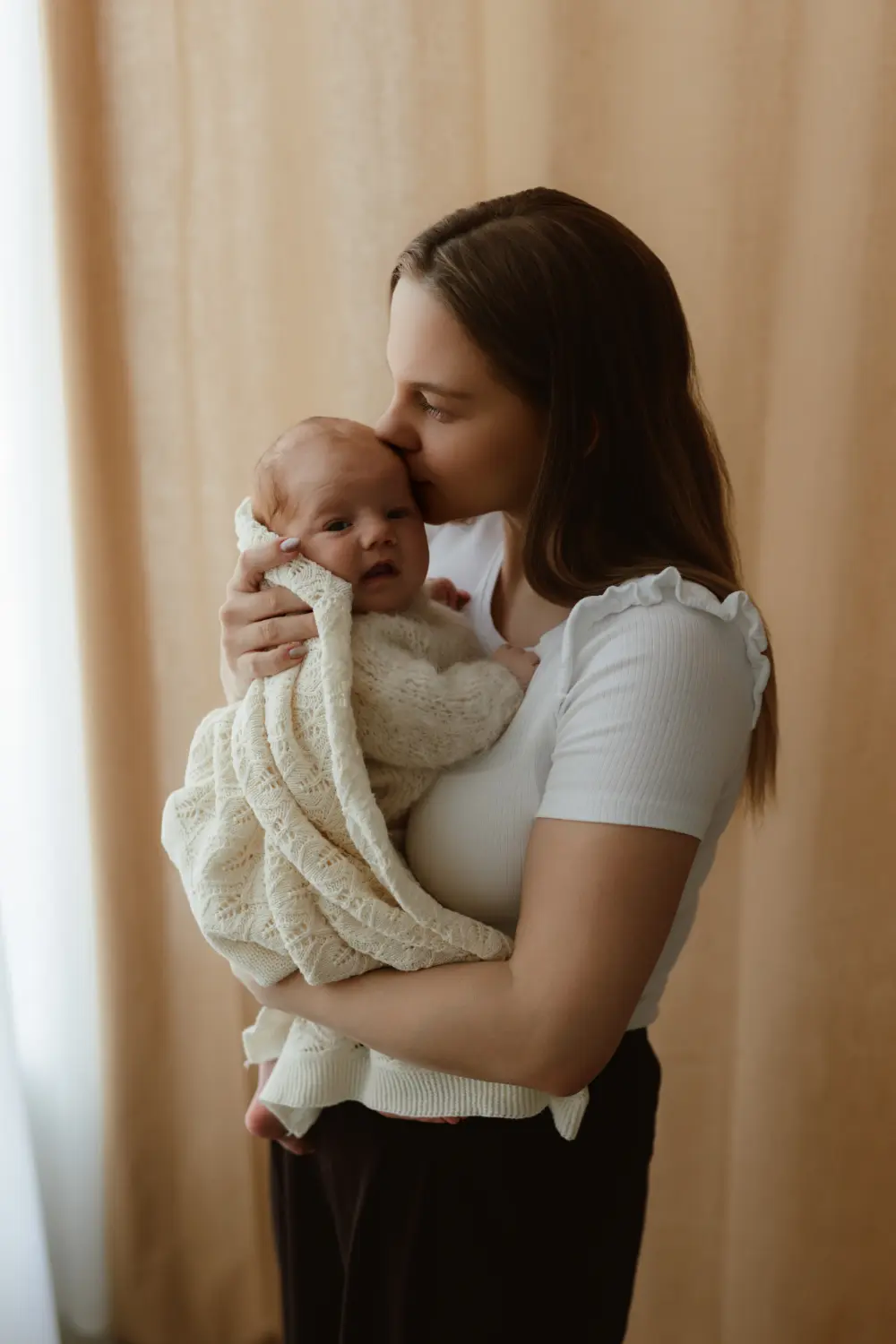 Matka bozkáva bábätko na hlavičku počas pokojného fotenia bábätiek v ateliéri v Nových Zámkoch