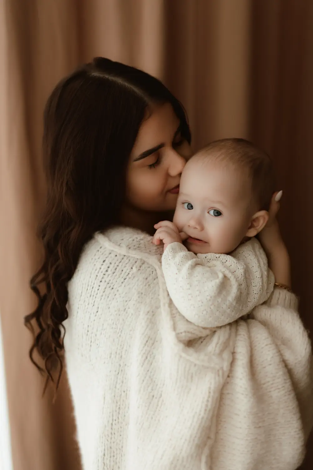  Mama drží svoje bábätko v náručí pričom mu privoniava k vlasom počas prirodzeného materského fotenia v ateliéri v Novách Zámkoch 
