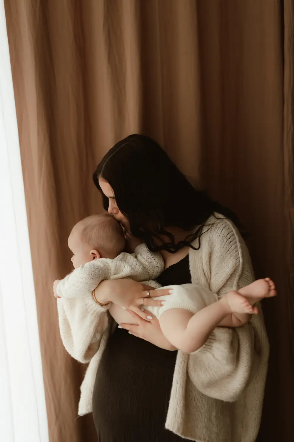 Mama bozkáva svoje bábätko počas emotívneho materského fotenia v ateliéri