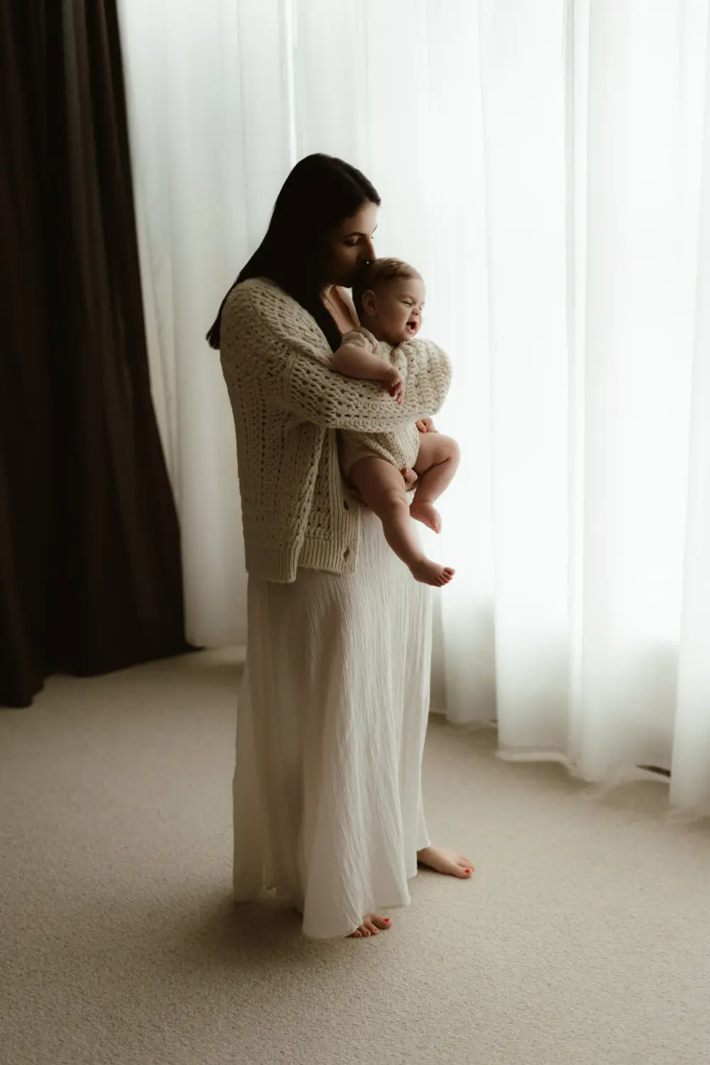  Mama nežne bozkáva bábätko na hlavu počas materského fotenia v ateliéri v Nových Zámkoch 