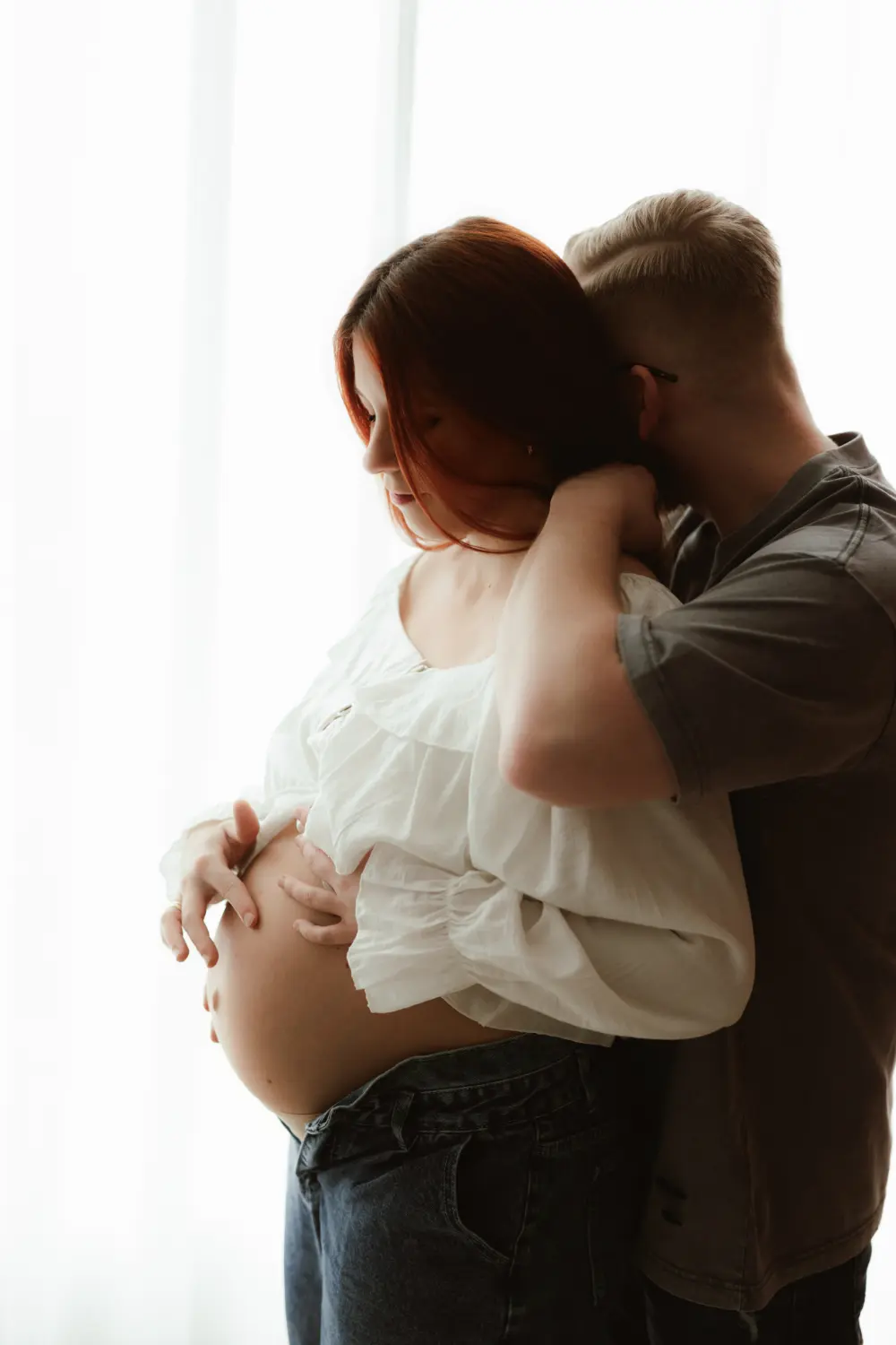 Uvoľnené tehotenské fotenie s pózovaním do protisvetla počas ktorého muž jemne objíma ženu počas ateliérového fotenia v Nitre