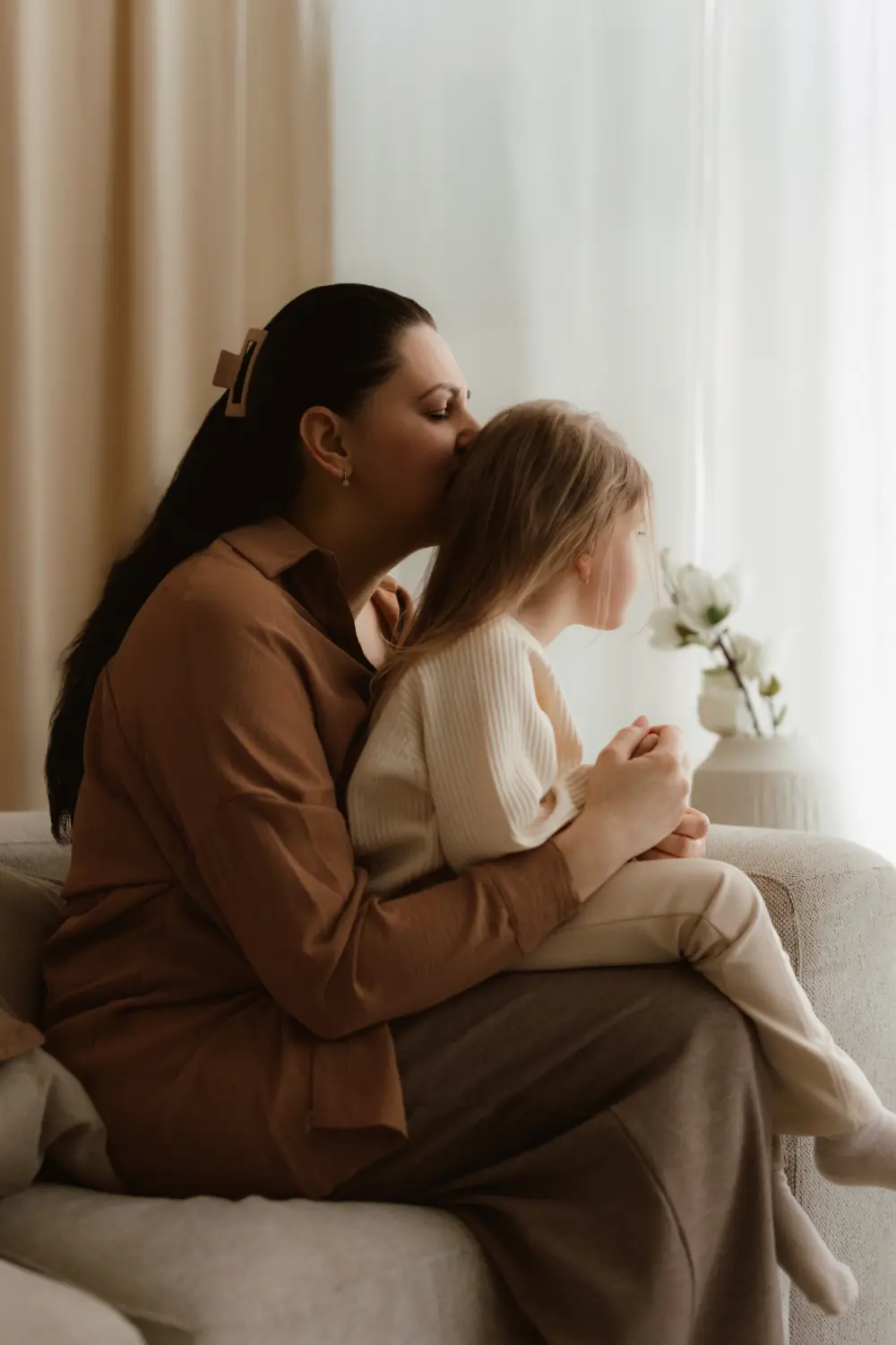  Mama bozkáva dieťa pričom ho drží v lone počas štýlového materského fotenia v ateliéri v Nitre 
