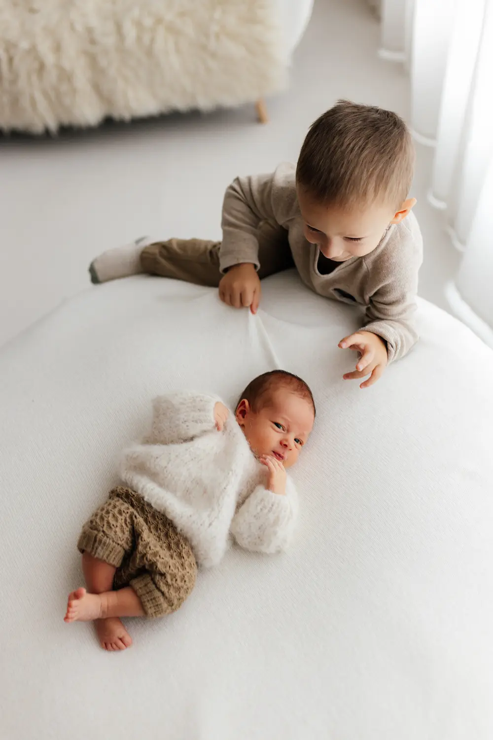 Starší súrodenec sa pozerá na novordenca počas newborn fotenia v ateliéri v Šuranoch