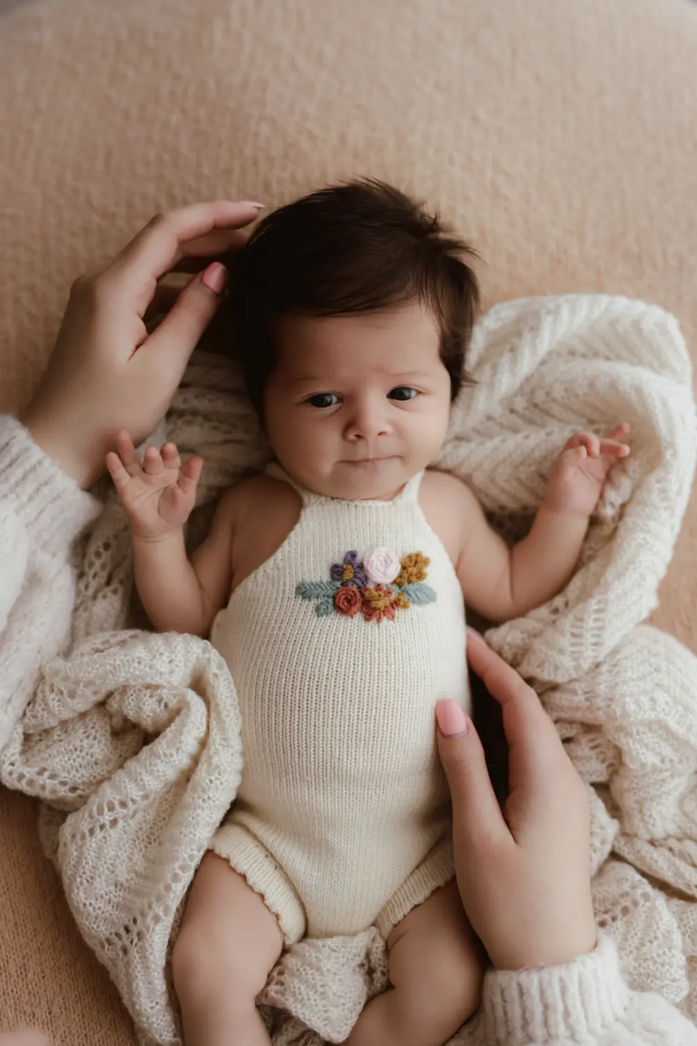 Ruky matky pridržiavajú bdelé bábätko počas bezpečného newborn fotenia v ateliéri v Nitre