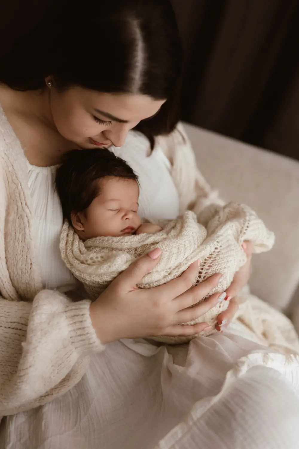 Matka nežne objíma svoje spiace bábätko pričom je zabalené v deke počas bezpečného newborn fotenia v ateliéri v Nitre