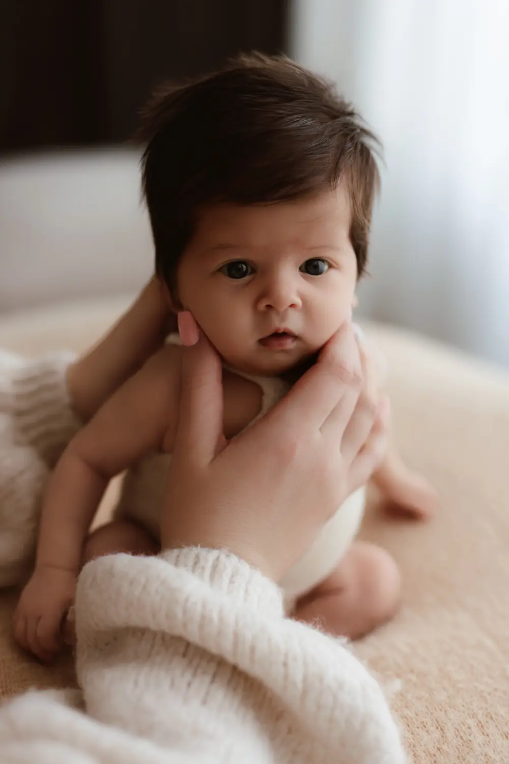 Dvojmesačné bábätko počas newborn fotenia polohované na ben bagu za pomoci ruk mami počas prirodzeného novorodeneckého fotenia v ateliéri v Nitre