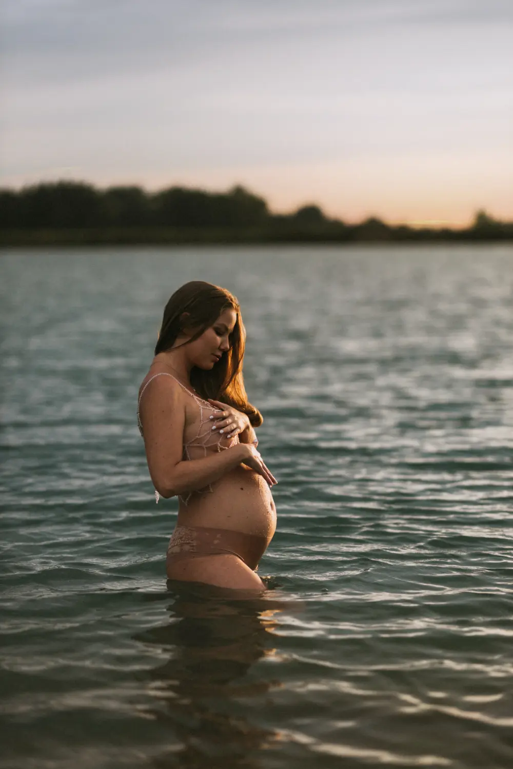 Tehotná žena pózuje vo vode pričom si jemne hladí tehotenské brucho počas tehotenského fotenia v Nitre