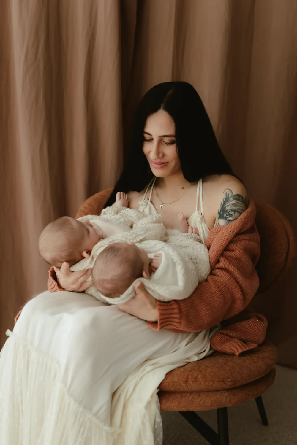 Mama sa láskavo pozerá na svoje spiace newborn dvojčatá počas bezpečného a prirodzeného newborn fotenia v ateliéri v Nitre