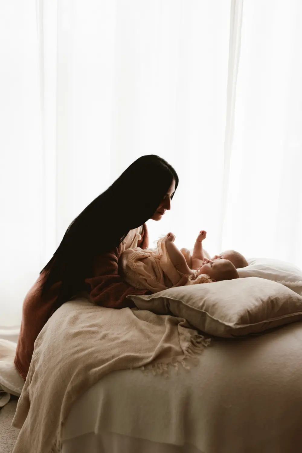 Matka sa pozerá na svoje bábätká pričom sa k nim prihovára a nežne ich pridržiava počas bezpečného newborn fotenia v ateliéri v Nitre