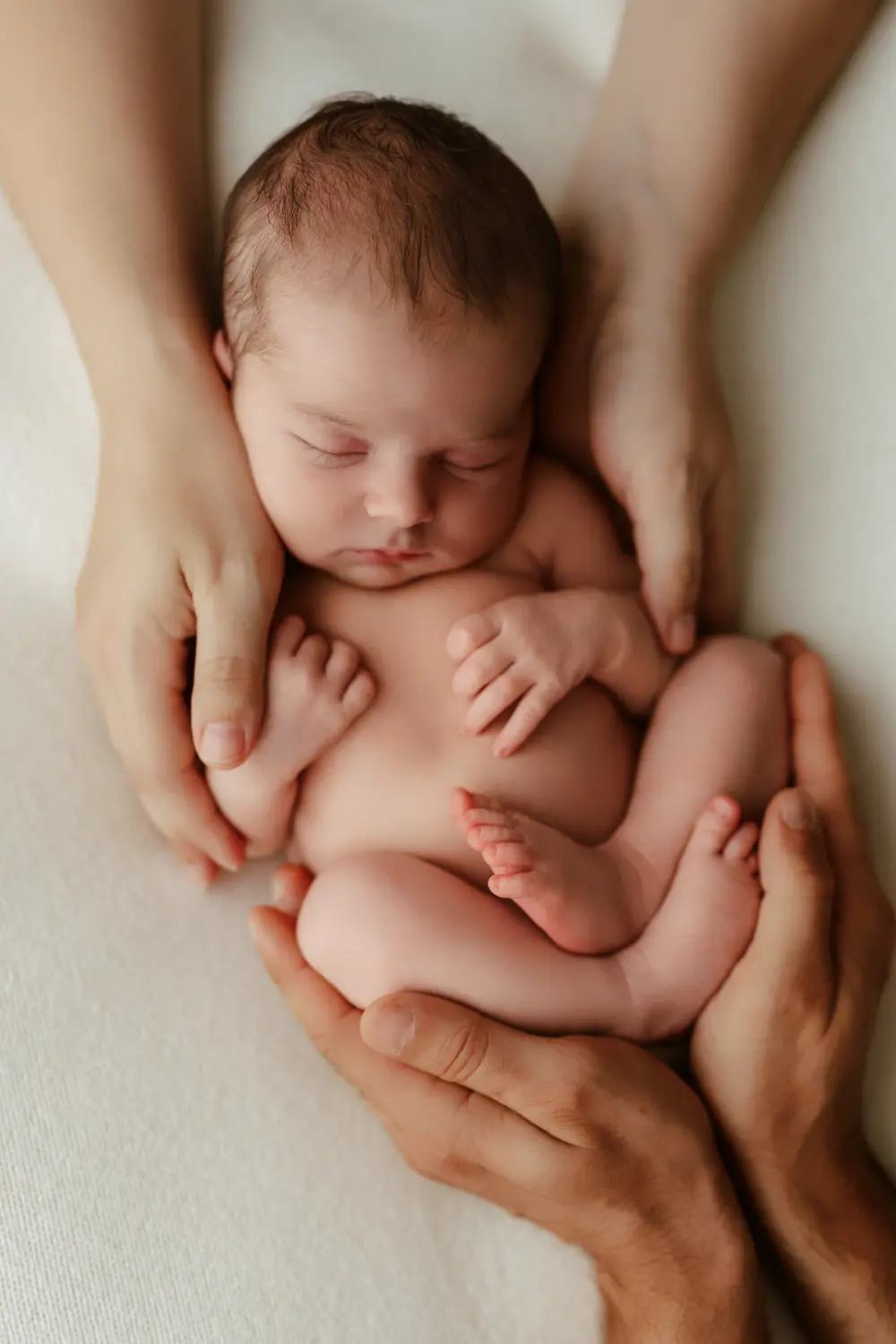 Rodičovské ruky prirdžiavajú spiace bäbätko počas newborn fotenia v ateliéri v Nitre.