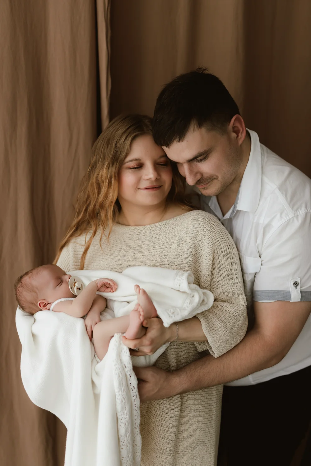 novorodenecke-fotenie-atelier-surany-zahraphoto-010 Rodičia šťastne držia svoje spiace bábätko počas newborn fotenia v ateliéri v Šuranoch